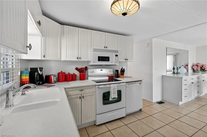 Kitchen with white appliances, light tile patterned floors, light countertops, and white cabinetry.  Open to ample dining area.