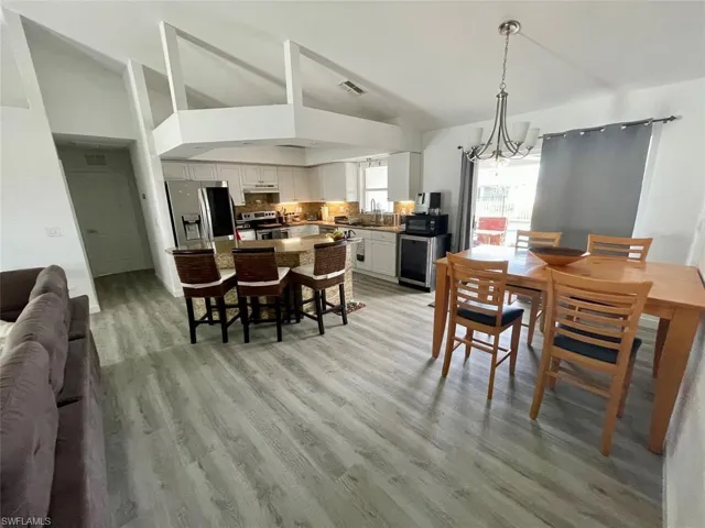 Dining area featuring an inviting chandelier, light wood finished floors, visible vents, and high vaulted ceiling