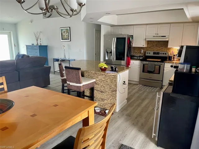 Kitchen featuring decorative backsplash, under cabinet range hood, light wood-type flooring, a notable chandelier, and stainless steel appliances