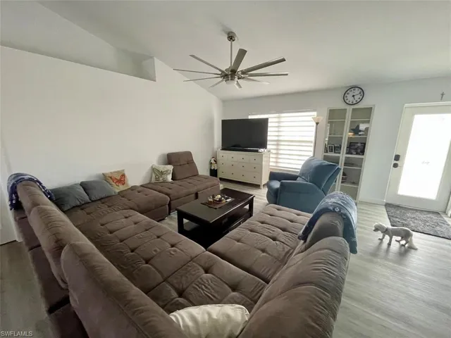 Living room with a ceiling fan, lofted ceiling, wood finished floors, and a healthy amount of sunlight