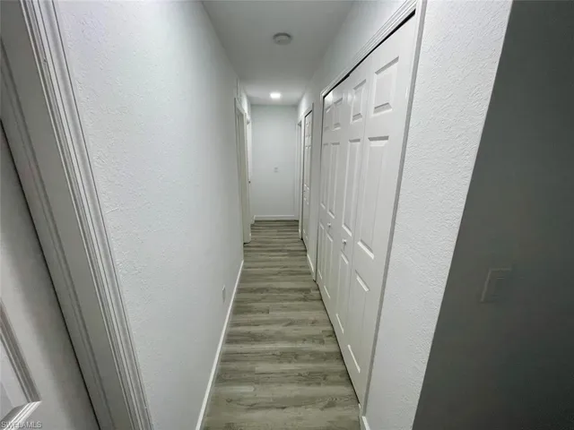 Hallway featuring baseboards, a textured wall, and wood finished floors