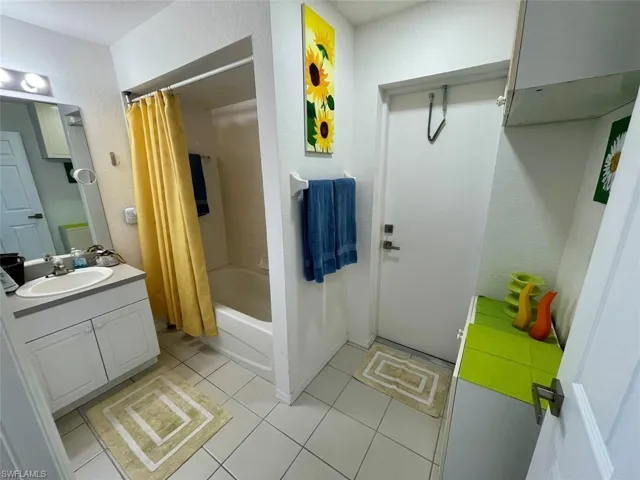 Full bath featuring tile patterned flooring, a textured wall, shower / bath combination with curtain, and vanity