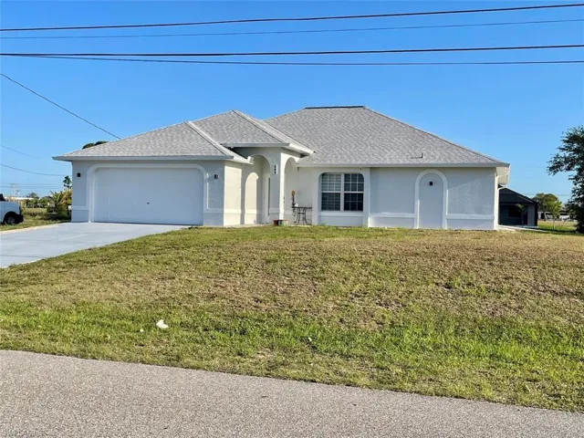 Ranch-style house featuring roof with shingles, an attached garage, a front lawn, stucco siding, and driveway