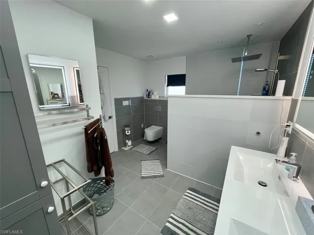 Bathroom featuring walk in shower, a sink, tile patterned flooring, double vanity, and tile walls