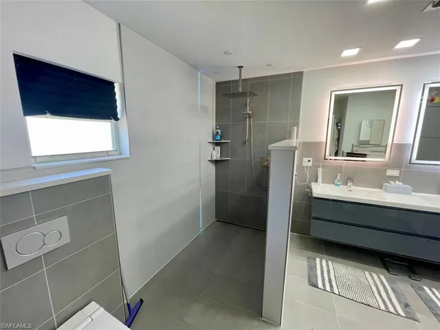 Bathroom featuring walk in shower, tile walls, tile patterned flooring, and vanity