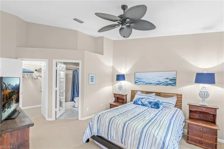 Bedroom with a spacious closet, light carpet, ceiling fan, and ensuite bath