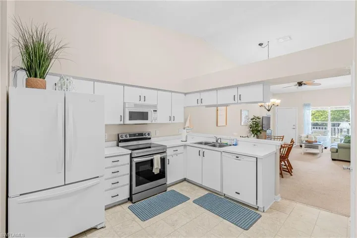 Kitchen with white appliances, high vaulted ceiling, light countertops, white cabinets, and light carpet