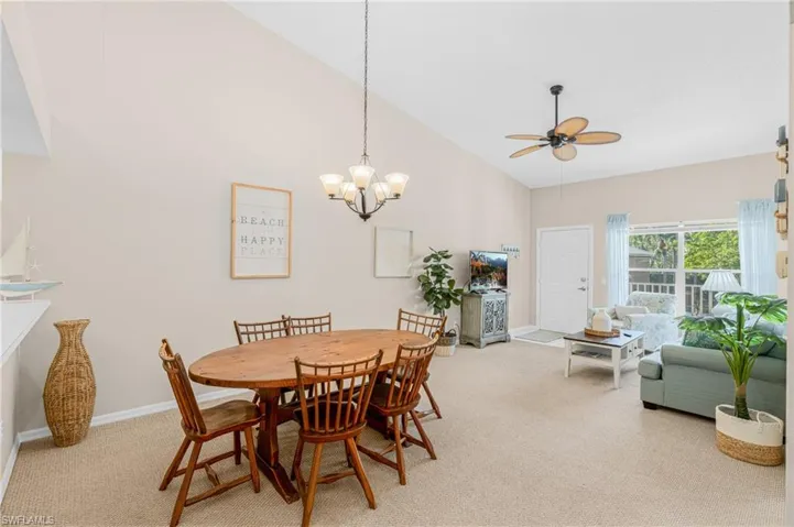 Carpeted dining area with high vaulted ceiling, a ceiling fan, and a chandelier