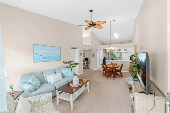 Carpeted living area featuring high vaulted ceiling, a ceiling fan, and a chandelier