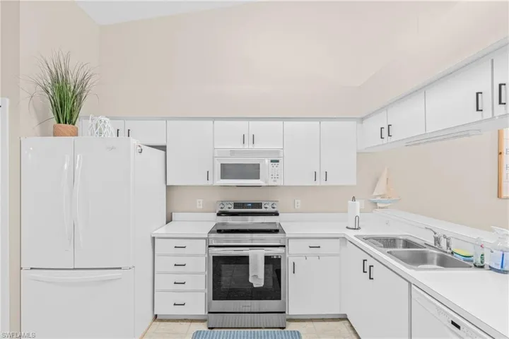 Kitchen featuring white appliances, light countertops, white cabinetry, and light tile patterned floors