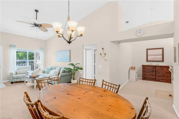 Dining area featuring light colored carpet, high vaulted ceiling, a ceiling fan, and a chandelier