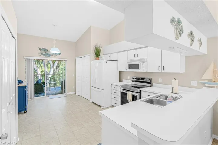 Kitchen with white appliances, light countertops, a towering ceiling, a peninsula, and hanging light fixtures