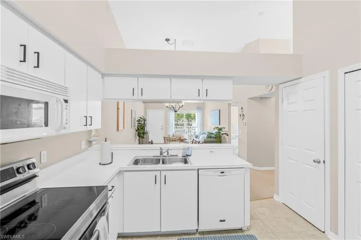 Kitchen with white appliances, white cabinets, light countertops, a high ceiling, and a chandelier