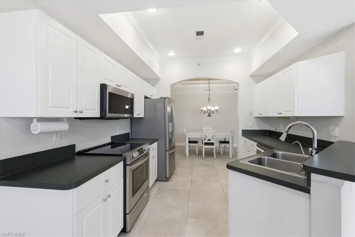 Bright kitchen featuring white cabinetry, dark countertops, stainless steel appliances, and a double basin sink