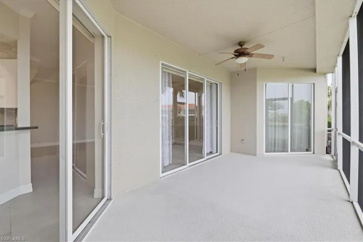 Expansive covered patio featuring a textured concrete floor, multiple sliding glass doors, a ceiling fan, and screened enclosures