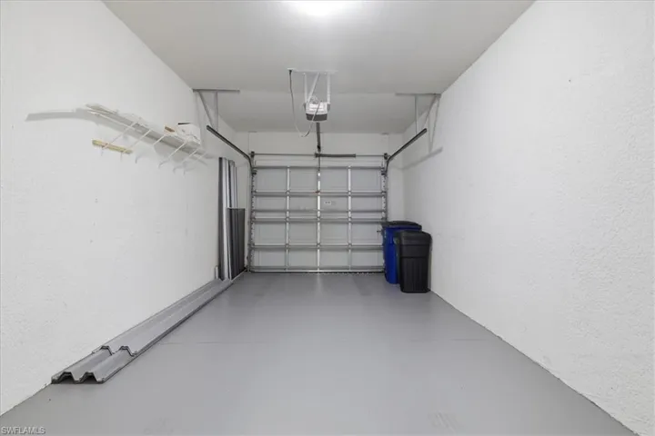 Single-bay garage featuring a light gray floor, white textured walls, and an overhead garage door opener