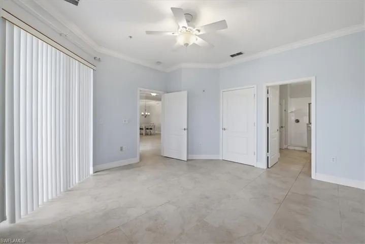 Spacious master bedroom featuring light blue walls, neutral tile flooring, crown molding, and a ceiling fan