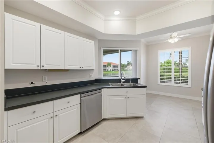 Kitchen featuring white cabinetry, dark countertops, a stainless steel dishwasher, and a dual-basin sink with a gooseneck faucet