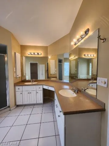 Full bath with double vanity, a stall shower, and light tile patterned floors