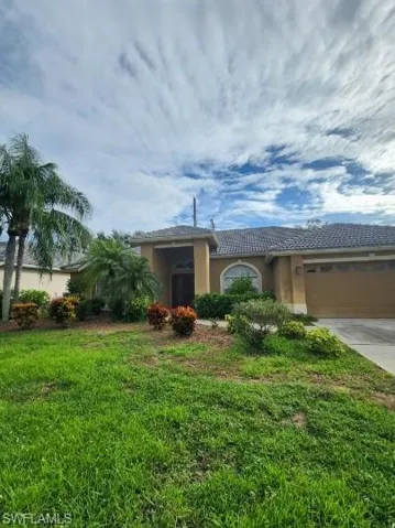 View of front facade with a garage, stucco siding, a front yard, driveway, and a tile roof