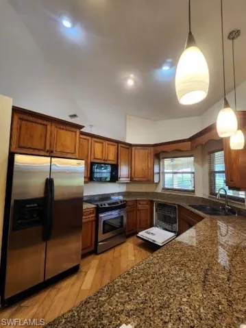 Kitchen with wood finish cabinetry, dark stone countertops, stainless steel appliances, pendant lighting, and light wood-style floors