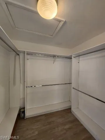Walk in closet with dark wood-style flooring and attic access
