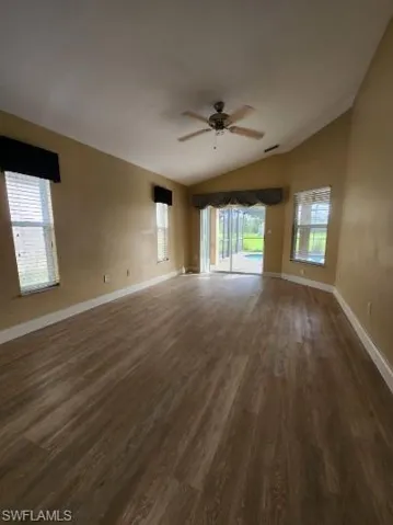 Empty room with dark wood-type flooring, a ceiling fan, and lofted ceiling