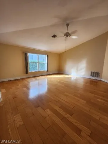 Spare room featuring light wood finished floors, ceiling fan, and lofted ceiling