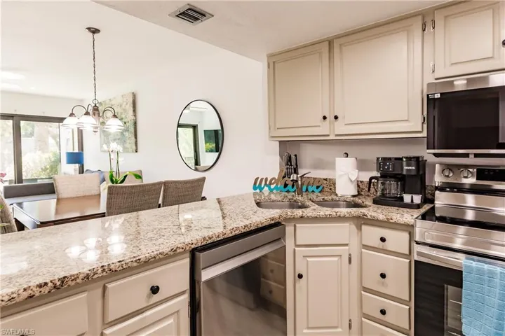 Kitchen with visible vents, light stone counters, stainless steel appliances, pendant lighting, and a sink