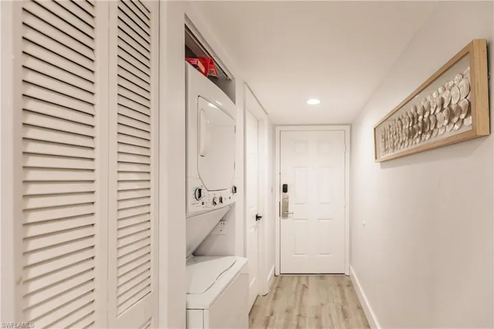 Clothes washing area with recessed lighting, light wood-style floors, stacked washer / dryer, laundry area, and baseboards