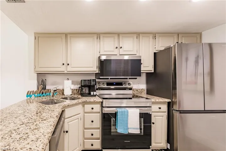 Kitchen featuring light stone countertops, visible vents, stainless steel appliances, and a sink