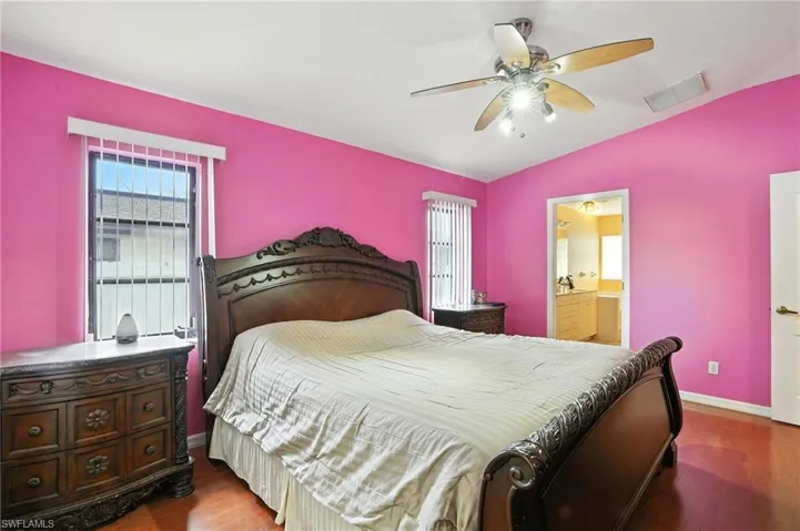Bedroom with wood finished floors, lofted ceiling, ensuite bathroom, and a ceiling fan