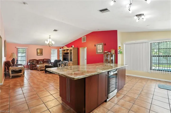 Kitchen with vaulted ceiling, light tile patterned flooring, wine cooler, a chandelier, and open floor plan