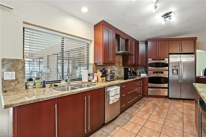 Kitchen featuring appliances with stainless steel finishes, decorative backsplash, light tile patterned flooring, a warming drawer, and wall chimney exhaust hood