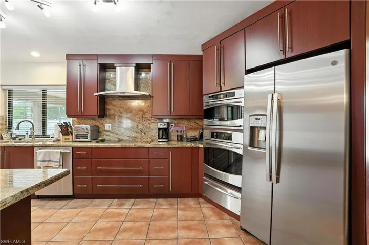 Kitchen featuring appliances with stainless steel finishes, a warming drawer, tasteful backsplash, light tile patterned flooring, and wall chimney exhaust hood