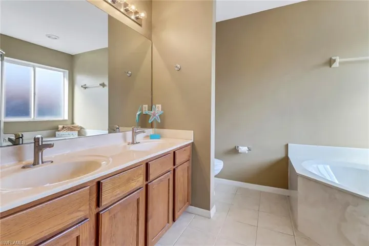 Bathroom featuring a bath, toilet, tile floors, and double sink vanity