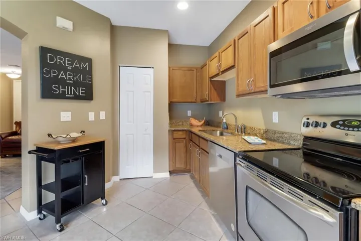 Kitchen featuring stainless steel appliances, sink, light stone countertops, and light tile flooring