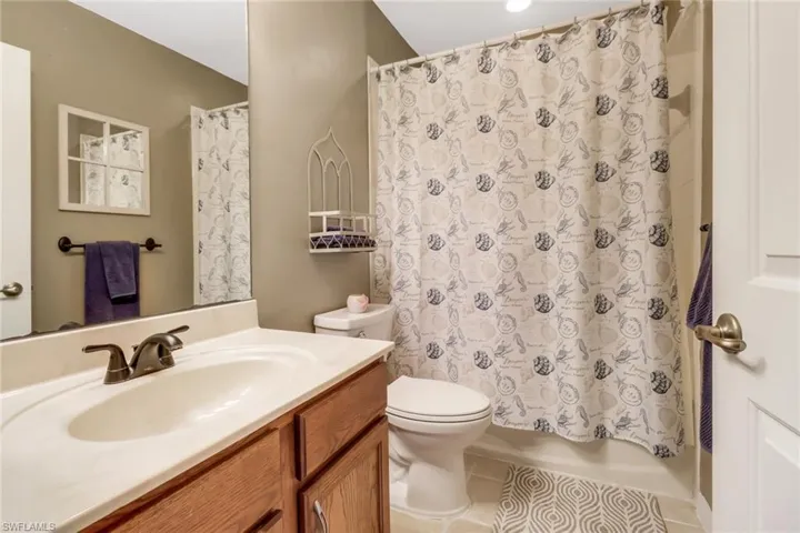 Full bathroom with shower / bath combo with shower curtain, vanity, toilet, and tile floors