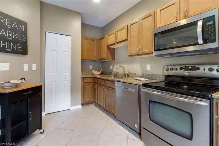 Kitchen with appliances with stainless steel finishes, light tile flooring, and light stone counters