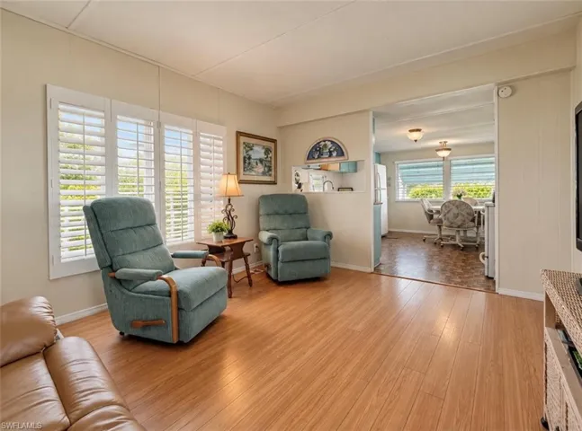 Living area featuring wood-finish flooring, white plantation shutters, and a wall cutout providing transparency to the internal space
