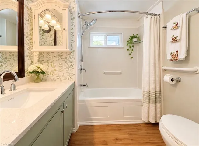 Bathroom featuring wood-finish flooring, a vanity with a solid-surface countertop and integrated sink, a built-in medicine cabinet, and a bathtub with a wall-mounted shower head and integrated grab bar