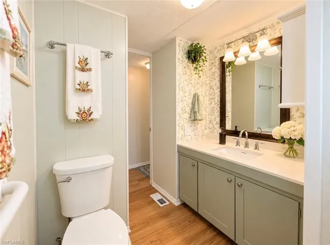 Bathroom featuring a vanity with sage green cabinetry, integrated countertop with sink, large wall-mounted mirror with a dark frame, four-light fixture, and wood-finish flooring