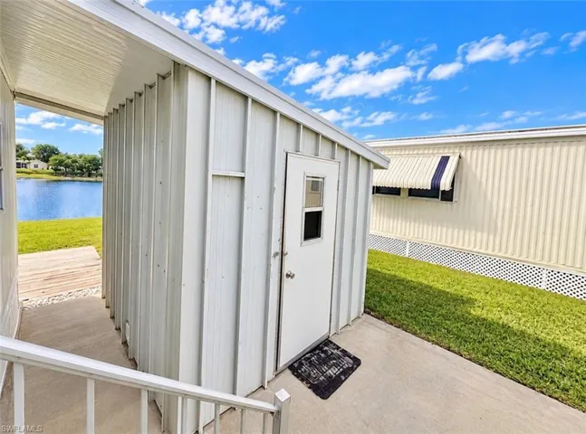 Metal-clad storage structure featuring a single door with a glass pane, concrete patio, and exterior lighting fixture