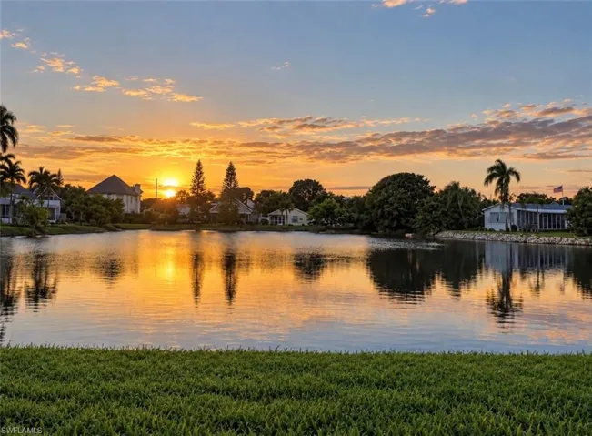 Waterfront property featuring a manicured lawn, mature palm trees, stone-reinforced shoreline, and expansive water frontage