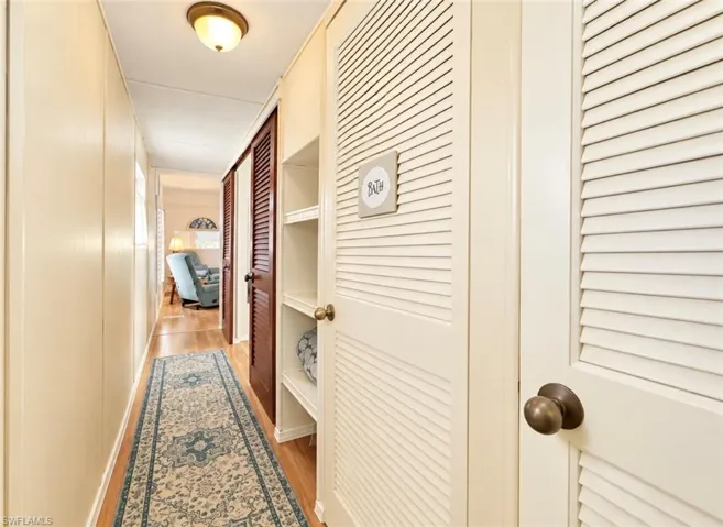 Interior hallway featuring wood-finish flooring, white louvered closet doors, and recessed shelving