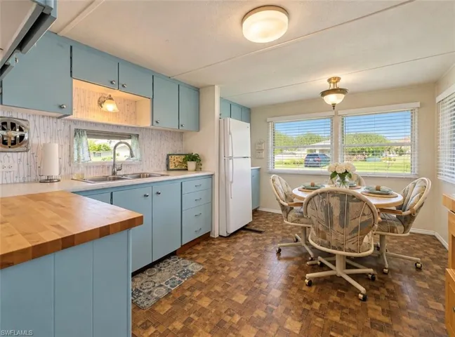 Kitchen featuring blue cabinetry, butcher block countertop, dual-basin stainless steel sink, large windows, and geometric tile-pattern flooring
