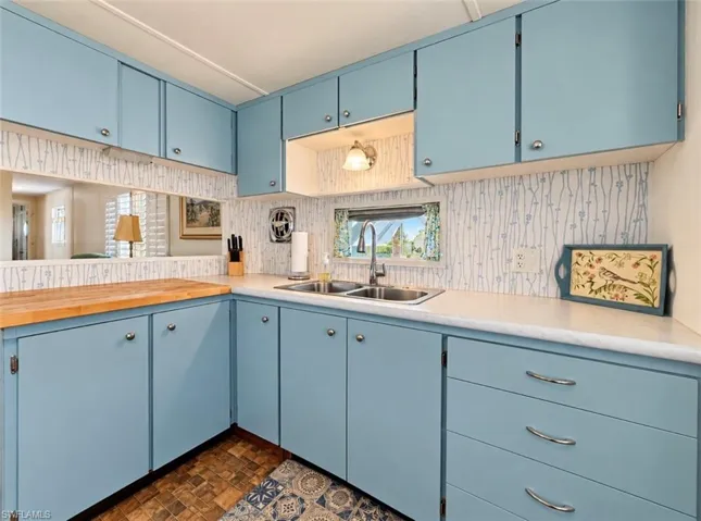 Kitchen featuring solid-color cabinetry, dual-basin stainless steel sink, wood-surface countertop, and patterned wall covering