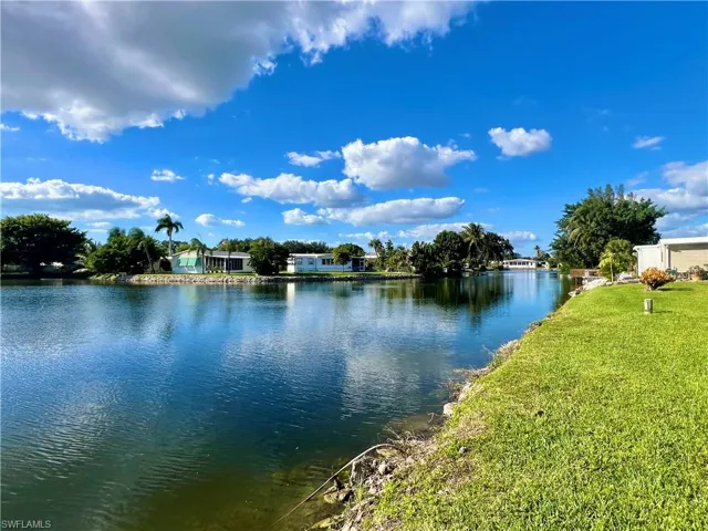 Waterfront property featuring a canal shoreline, expansive grass lawn, rock-lined embankment, and established palm trees