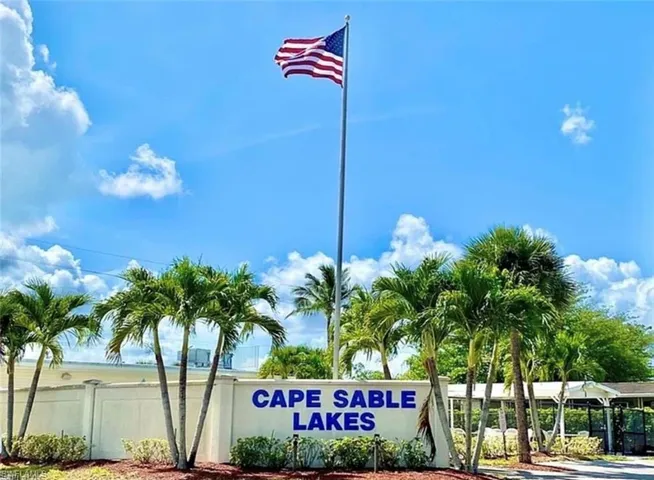 Concrete perimeter wall featuring professional signage, mature palm trees, and a tall central flagpole