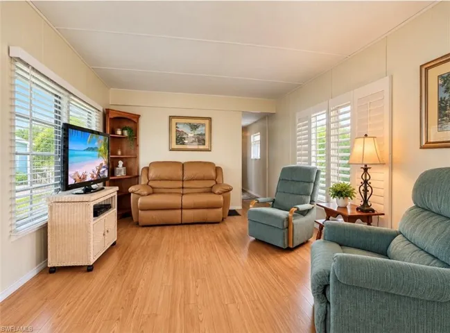 Living area featuring wood-finish flooring, built-in corner shelving, and large windows with integrated plantation-style shutters